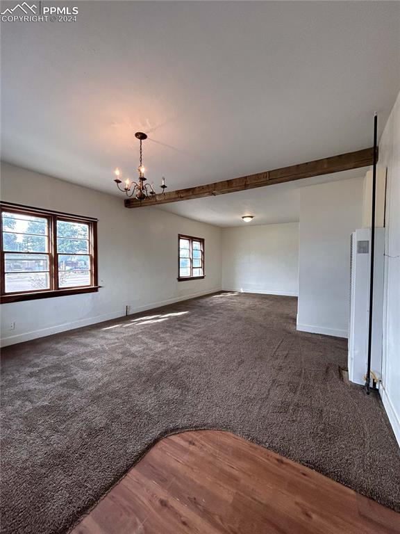 carpeted spare room with an inviting chandelier, a wealth of natural light, and beam ceiling