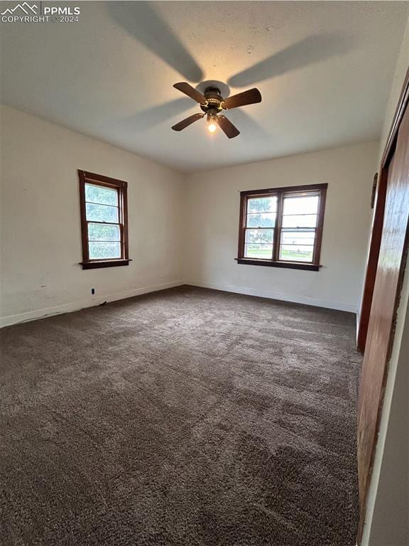 unfurnished room featuring a healthy amount of sunlight, dark colored carpet, and ceiling fan