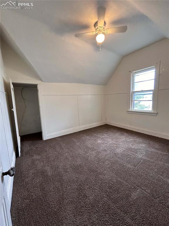 additional living space featuring vaulted ceiling, dark colored carpet, and ceiling fan