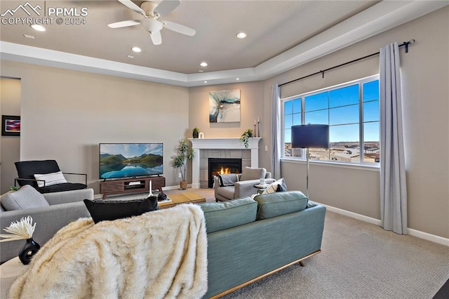 living room featuring a tray ceiling, carpet, ceiling fan, and a tile fireplace