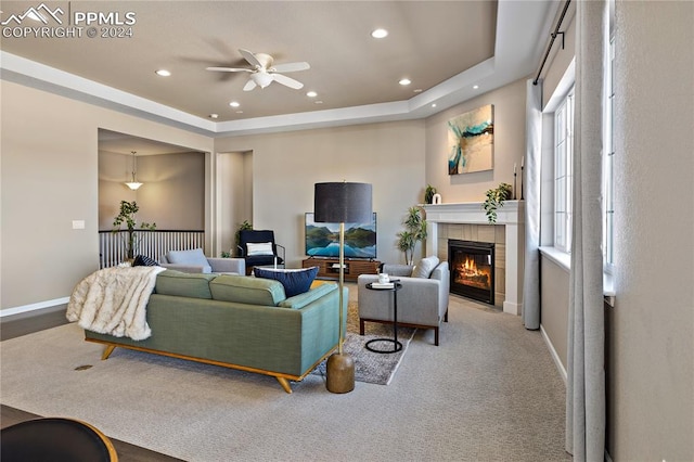 carpeted living room featuring a tray ceiling, ceiling fan, and a tile fireplace