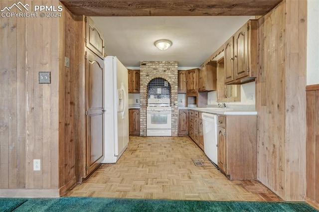 kitchen featuring light parquet flooring, white appliances, wooden walls, and sink