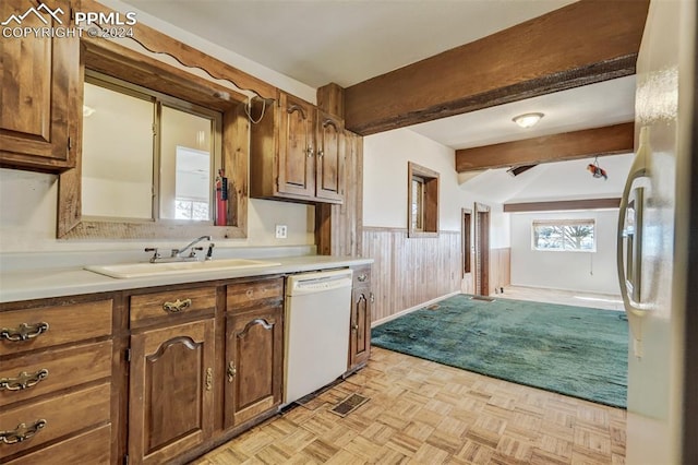 kitchen with beamed ceiling, sink, wood walls, white appliances, and light parquet floors