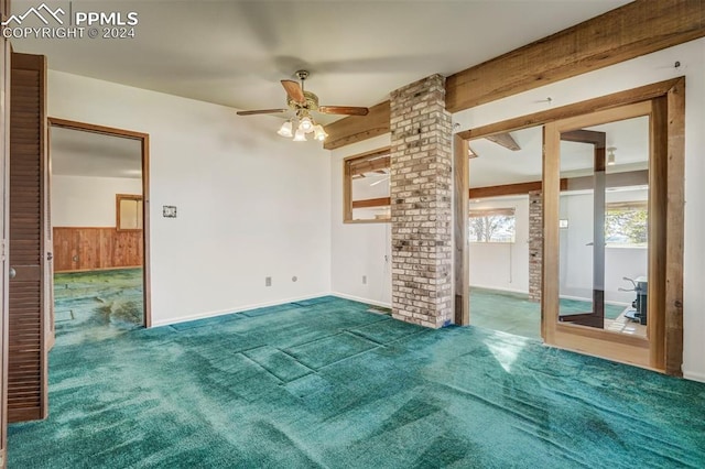 carpeted empty room featuring decorative columns, beamed ceiling, wood walls, and ceiling fan