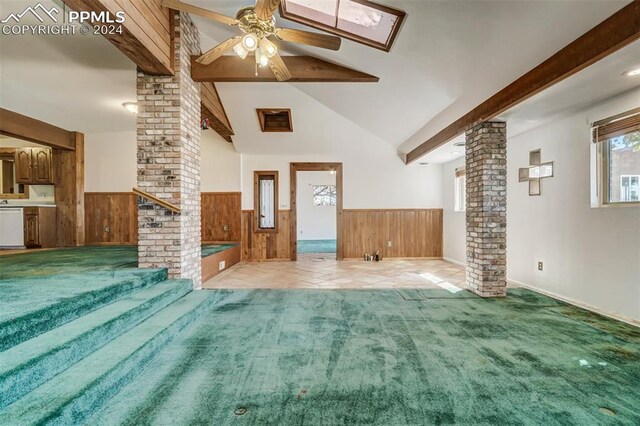 unfurnished living room with light carpet, wooden walls, lofted ceiling with skylight, ceiling fan, and ornate columns