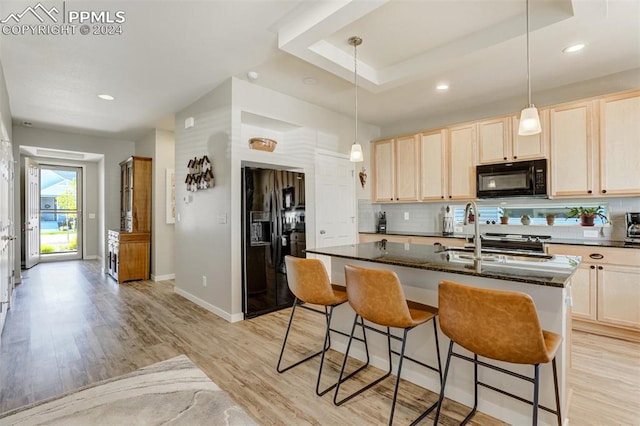 kitchen featuring an island with sink, black appliances, decorative light fixtures, and light hardwood / wood-style flooring