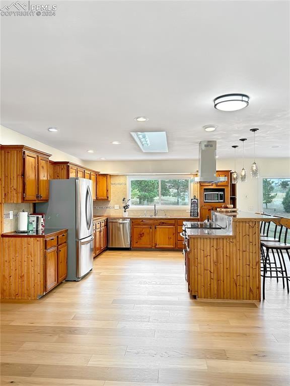 kitchen with a kitchen island, exhaust hood, stainless steel appliances, light wood-type flooring, and decorative light fixtures