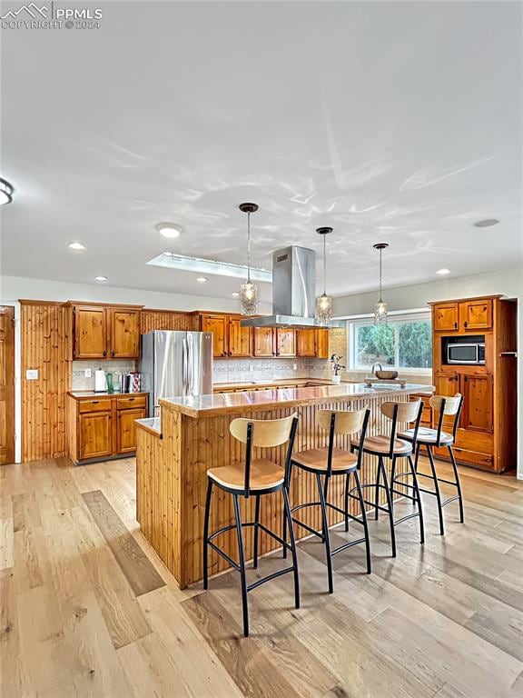 kitchen with appliances with stainless steel finishes, light hardwood / wood-style floors, a kitchen island, and pendant lighting