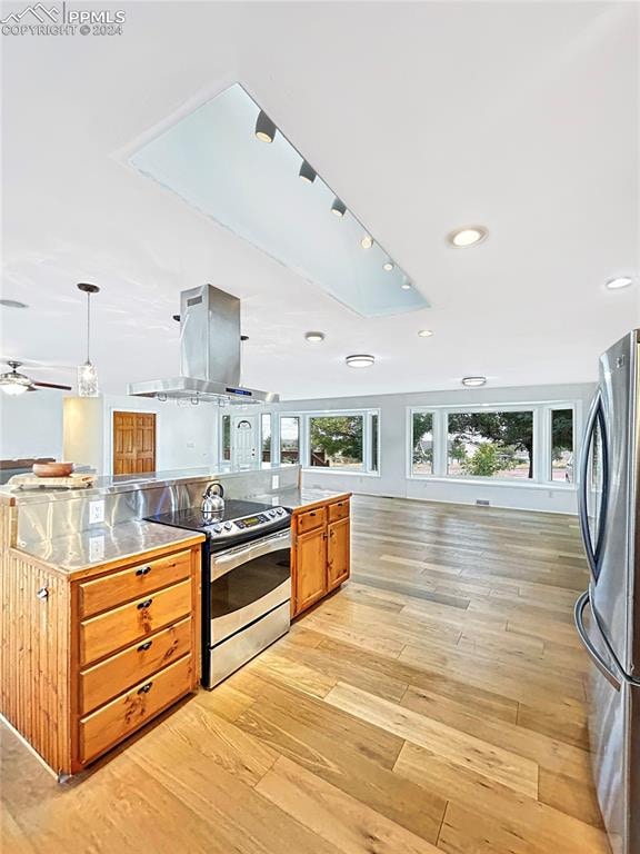 kitchen featuring stainless steel appliances, light wood-type flooring, ceiling fan, range hood, and decorative light fixtures