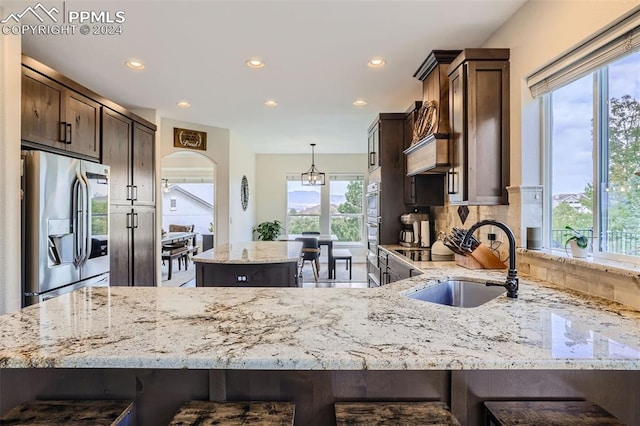 kitchen featuring light stone countertops, stainless steel appliances, sink, kitchen peninsula, and backsplash