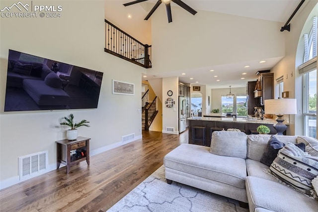 living room with ceiling fan, high vaulted ceiling, plenty of natural light, and wood-type flooring