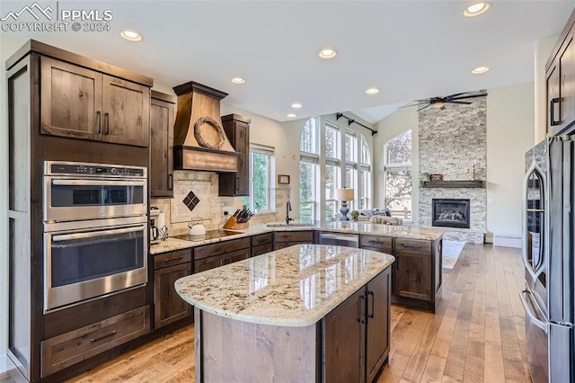 kitchen with light stone counters, ceiling fan, a stone fireplace, appliances with stainless steel finishes, and light hardwood / wood-style floors