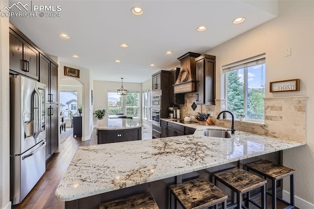 kitchen with sink, kitchen peninsula, pendant lighting, custom exhaust hood, and appliances with stainless steel finishes