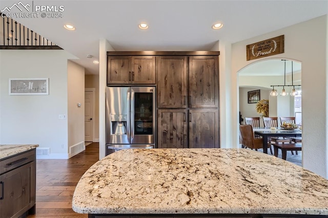 kitchen featuring stainless steel fridge, a kitchen island, light stone countertops, and dark wood-type flooring