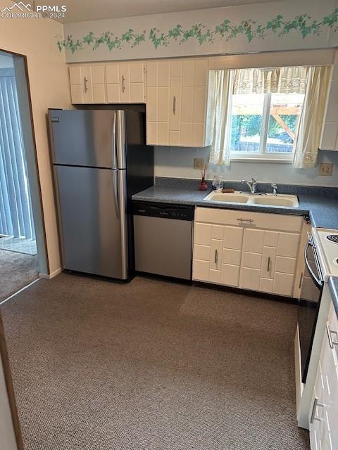 kitchen with sink, dark carpet, stainless steel appliances, and white cabinets