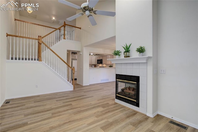 unfurnished living room featuring ceiling fan, light hardwood / wood-style flooring, a towering ceiling, and a tile fireplace