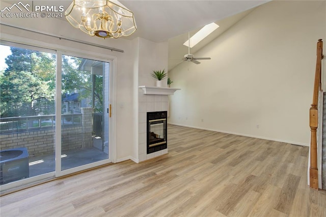 unfurnished living room with ceiling fan with notable chandelier, wood-type flooring, a tiled fireplace, and a skylight