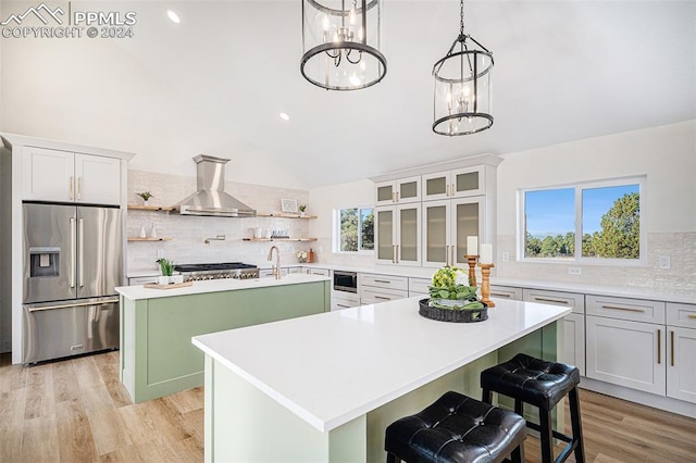 kitchen featuring tasteful backsplash, stainless steel appliances, lofted ceiling, a center island with sink, and wall chimney range hood