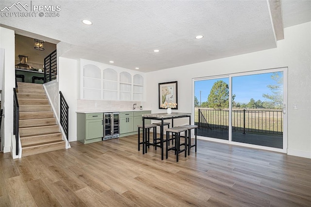 dining room featuring a textured ceiling, indoor wet bar, light hardwood / wood-style floors, and beverage cooler