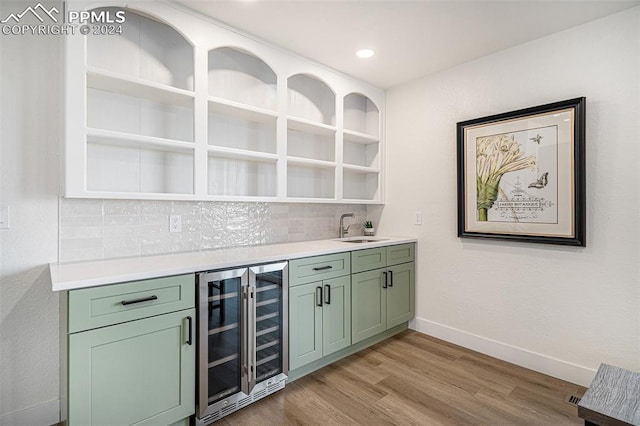 bar featuring wine cooler, sink, light hardwood / wood-style flooring, green cabinets, and decorative backsplash