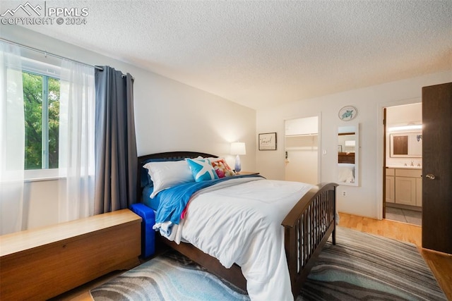 bedroom featuring connected bathroom, a textured ceiling, hardwood / wood-style floors, and sink