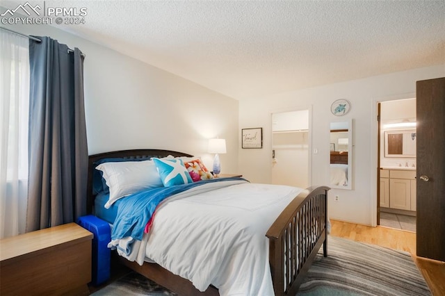 bedroom featuring a textured ceiling, hardwood / wood-style flooring, a closet, a spacious closet, and ensuite bathroom