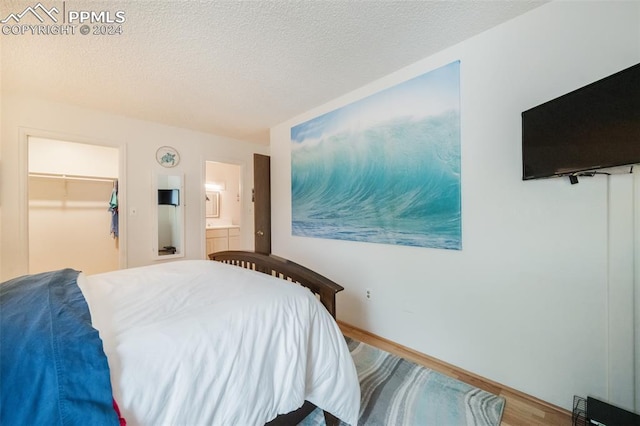 bedroom with wood-type flooring, a closet, a textured ceiling, ensuite bathroom, and a spacious closet