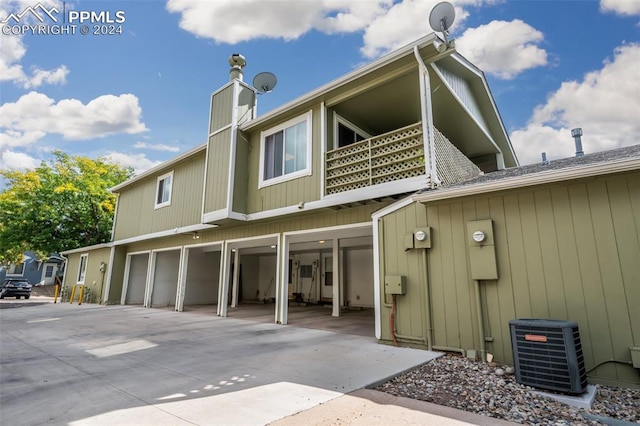 back of property with central AC unit, a garage, and a balcony