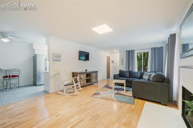 living room featuring ceiling fan, a fireplace, and light hardwood / wood-style floors