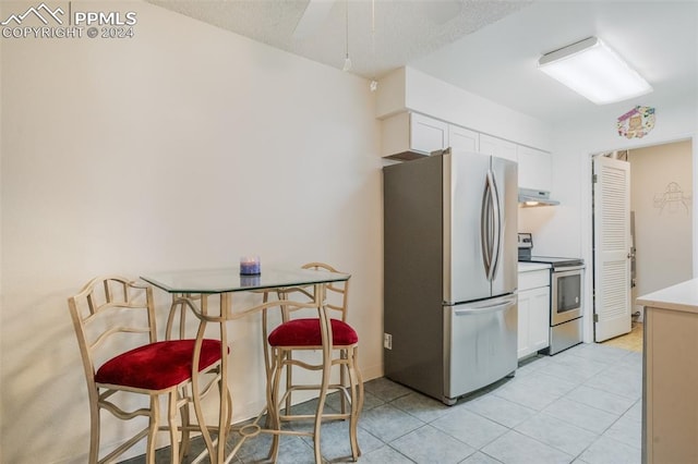 kitchen featuring appliances with stainless steel finishes, light tile patterned flooring, exhaust hood, and white cabinets