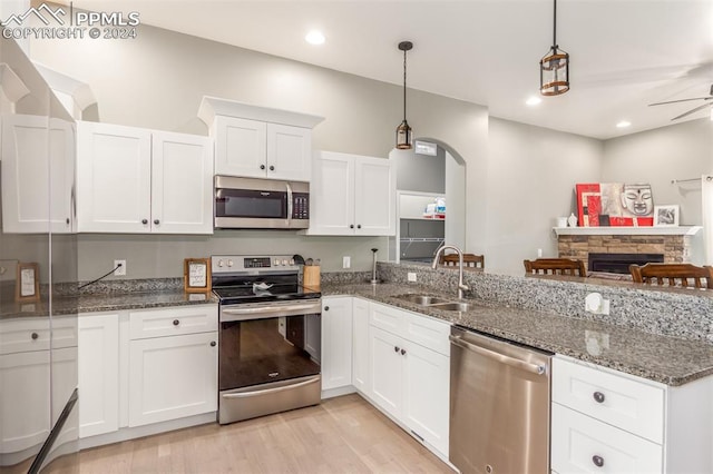 kitchen featuring white cabinets, a stone fireplace, stainless steel appliances, ceiling fan, and decorative light fixtures