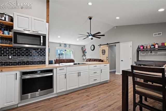 kitchen with light wood-type flooring, white cabinets, lofted ceiling, a barn door, and appliances with stainless steel finishes