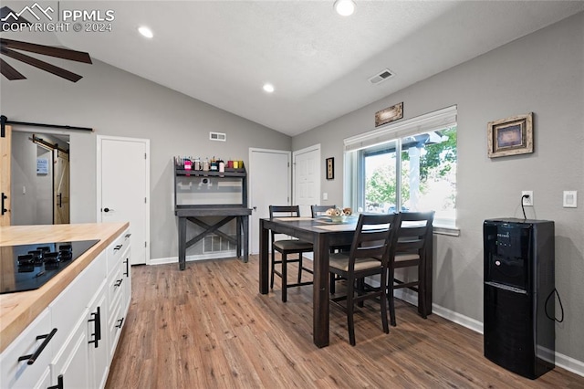 dining space with lofted ceiling, light hardwood / wood-style floors, ceiling fan, and a barn door