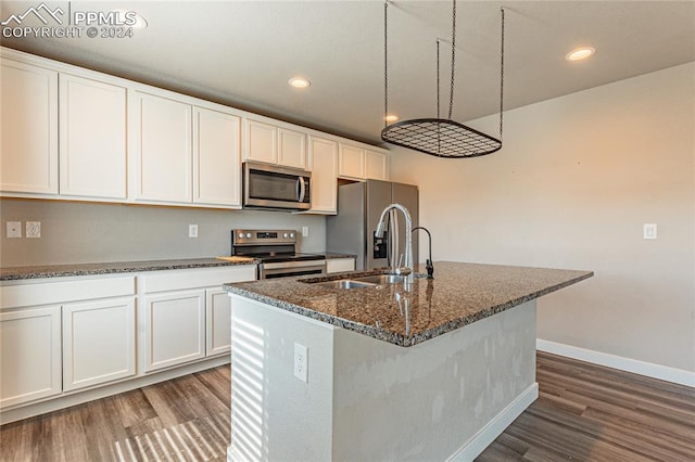 kitchen featuring dark stone counters, stainless steel appliances, white cabinets, and a center island with sink