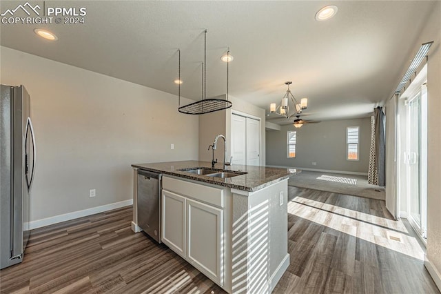 kitchen featuring sink, a center island with sink, dark wood-type flooring, stainless steel appliances, and dark stone counters