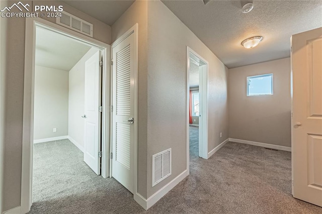 hall with a textured ceiling and light carpet