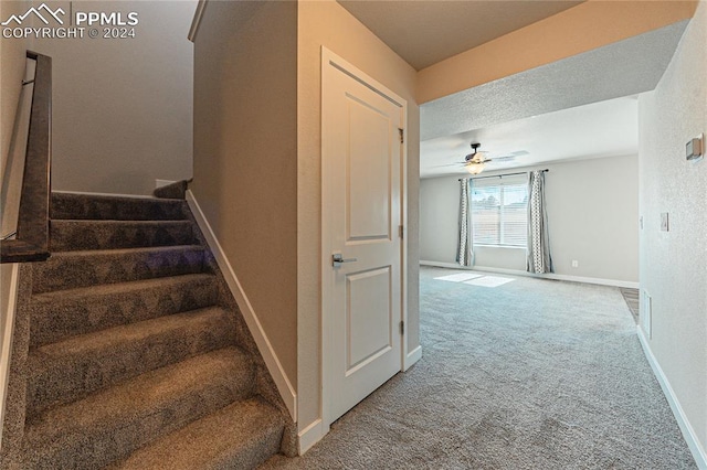 stairs with ceiling fan, a textured ceiling, and carpet