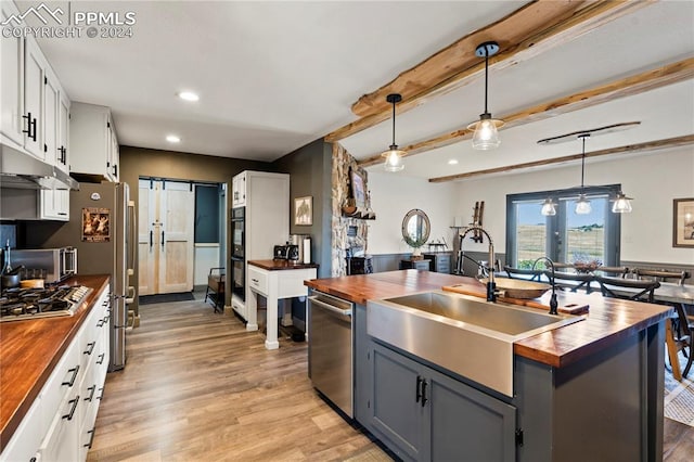 kitchen featuring hanging light fixtures, butcher block countertops, light hardwood / wood-style flooring, white cabinetry, and stainless steel appliances