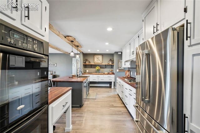 kitchen with white cabinets, hanging light fixtures, light hardwood / wood-style flooring, appliances with stainless steel finishes, and butcher block countertops