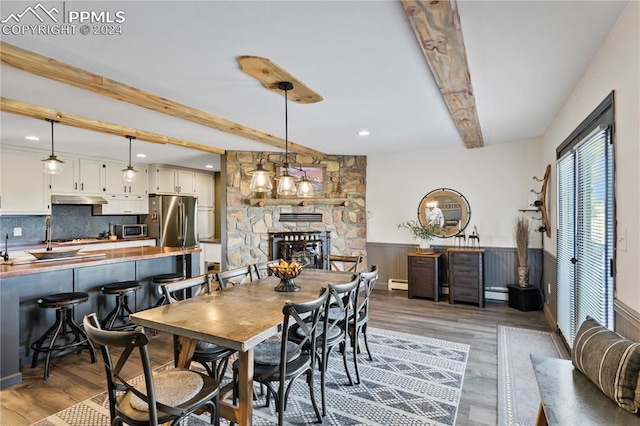 dining room featuring a baseboard heating unit, a stone fireplace, hardwood / wood-style flooring, and beamed ceiling