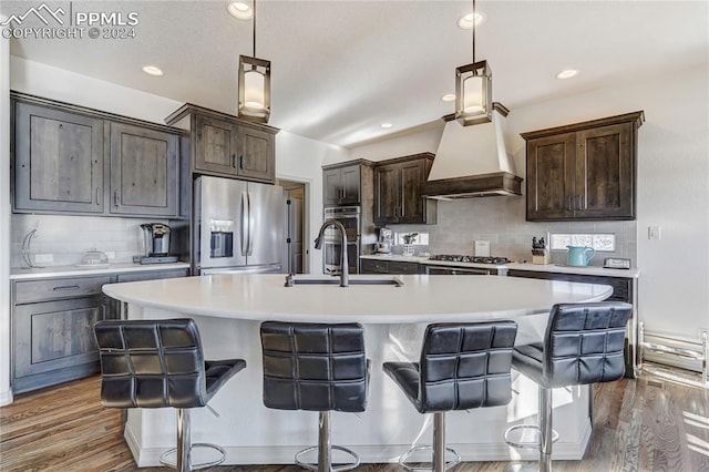 kitchen featuring appliances with stainless steel finishes, dark hardwood / wood-style flooring, custom range hood, sink, and a center island with sink