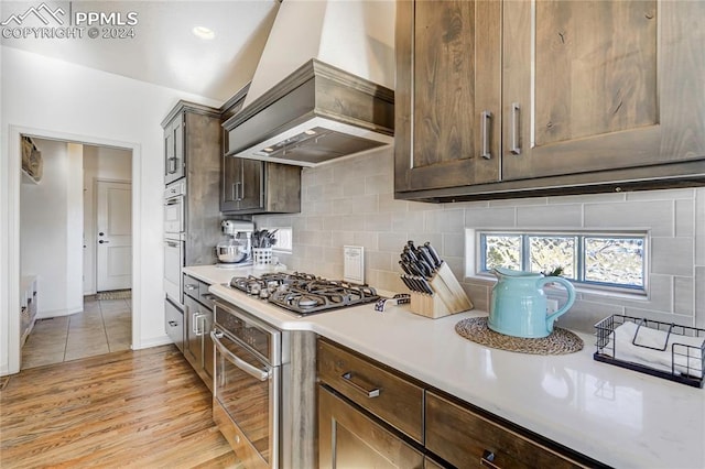 kitchen featuring stainless steel gas stovetop, premium range hood, light wood-type flooring, tasteful backsplash, and dark brown cabinetry