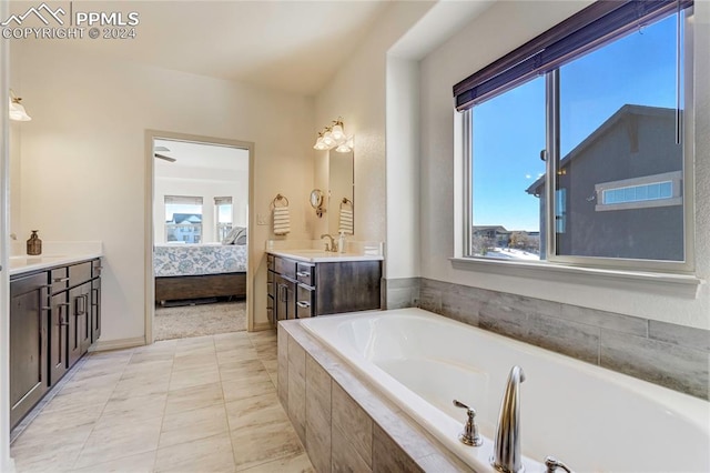 bathroom with tile patterned floors, tiled tub, plenty of natural light, and vanity