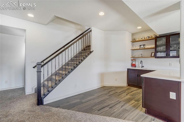 bar with sink, dark brown cabinetry, and dark wood-type flooring