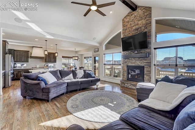 living room featuring beamed ceiling, wood-type flooring, ceiling fan, and a fireplace