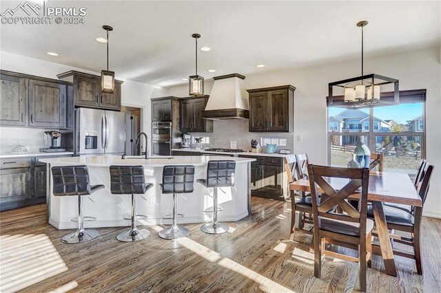 kitchen featuring pendant lighting, custom exhaust hood, stainless steel appliances, and a kitchen island with sink