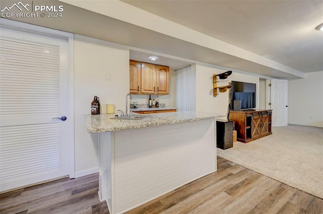 kitchen with light stone countertops, kitchen peninsula, sink, and hardwood / wood-style flooring