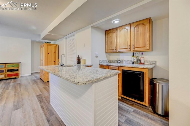 kitchen featuring light wood-type flooring, a center island, sink, beverage cooler, and light stone countertops