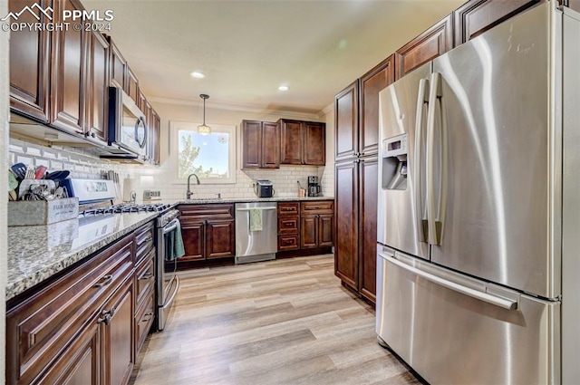 kitchen featuring light stone counters, stainless steel appliances, light hardwood / wood-style flooring, decorative light fixtures, and sink