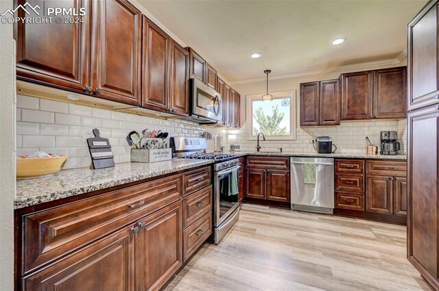 kitchen featuring ornamental molding, pendant lighting, stainless steel appliances, and light hardwood / wood-style flooring